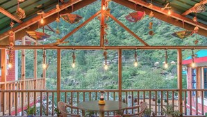 Un espace extérieur aménagé, abrité et doté de tables et de chaises, entouré de plantes en pot et offrant une vue sur un paysage verdoyant.