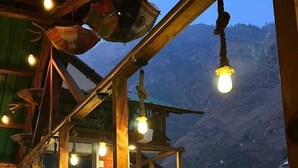 Une terrasse en bois avec une rambarde, un escalier et des luminaires suspendus.