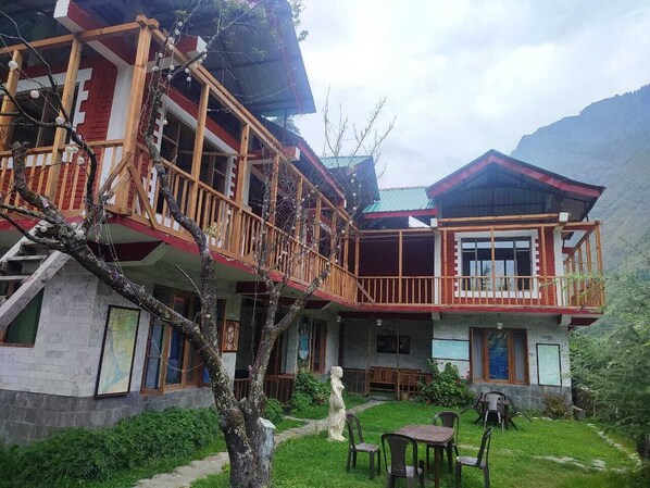 A two-story building with a balcony, a stone facade, and a garden area with chairs and a table.