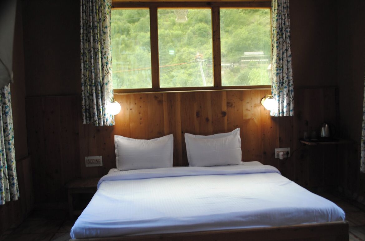 A wooden room with a bed, two bedside lamps, and a window with curtains.