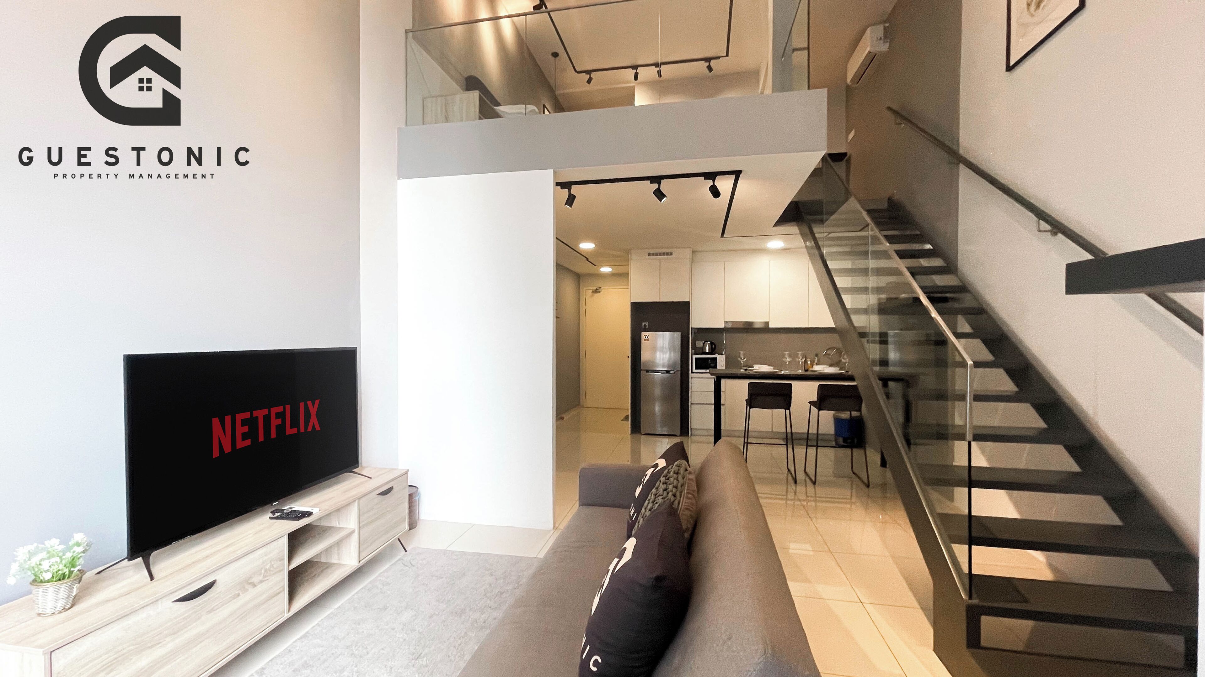 A modern living room with a flat-screen TV, a sofa, and a staircase leading to an upper level.