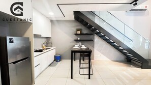 Una cocina moderna con un refrigerador empotrado, una mesa de comedor lista para cuatro personas y una escalera que conduce a un nivel superior.