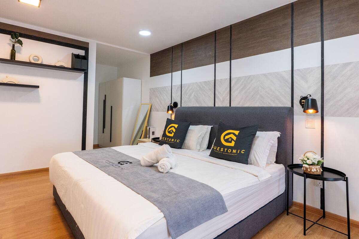 Une chambre d’hôtel moderne dotée d’un grand lit, d’une table de chevet, d’une étagère murale agrémentée d’objets décoratifs et d’un design original pour la tête de lit.