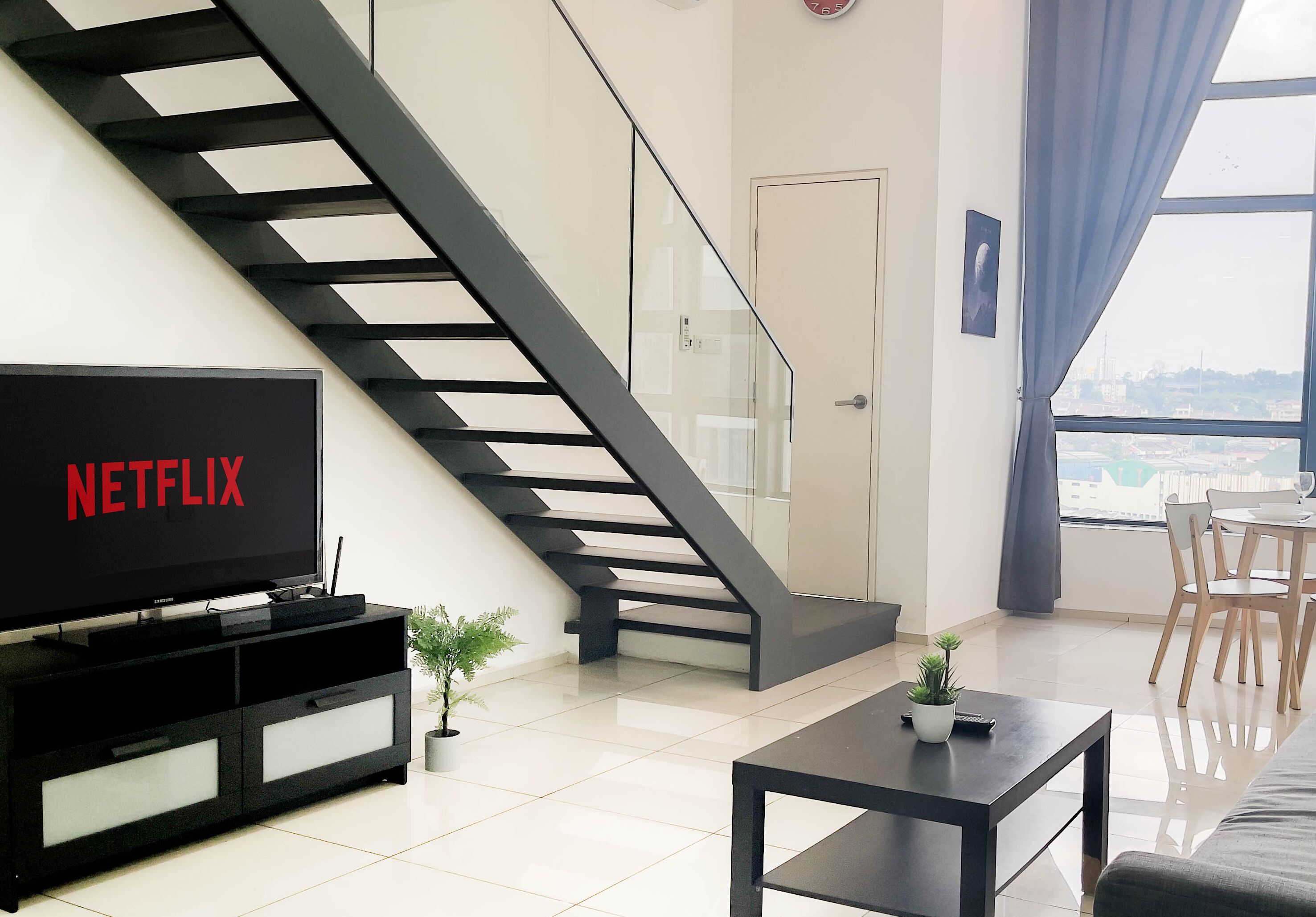 Un salon moderne avec un escalier, un téléviseur à écran plat, un coin repas et une vue sur la ville.