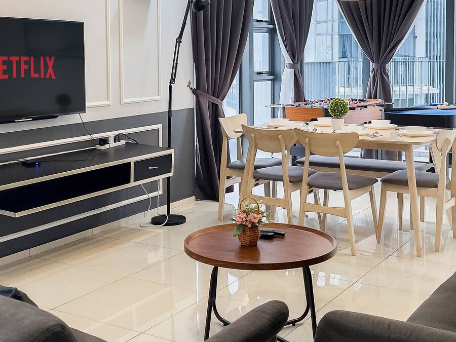 A modern living room with a flat-screen TV displaying 'NETFLIX', a dining area with a pool table, and a large window with curtains.