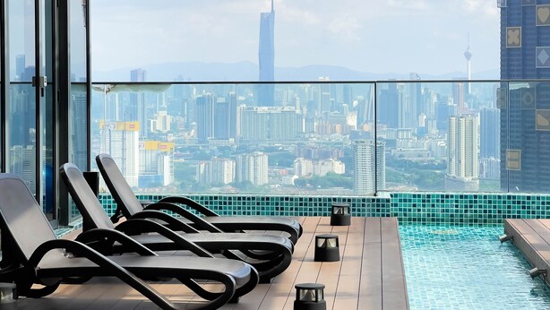 A rooftop pool area with lounge chairs and a cityscape view. - Guestonic EkoCheras Cozy Studio (Kuala Lumpur)
