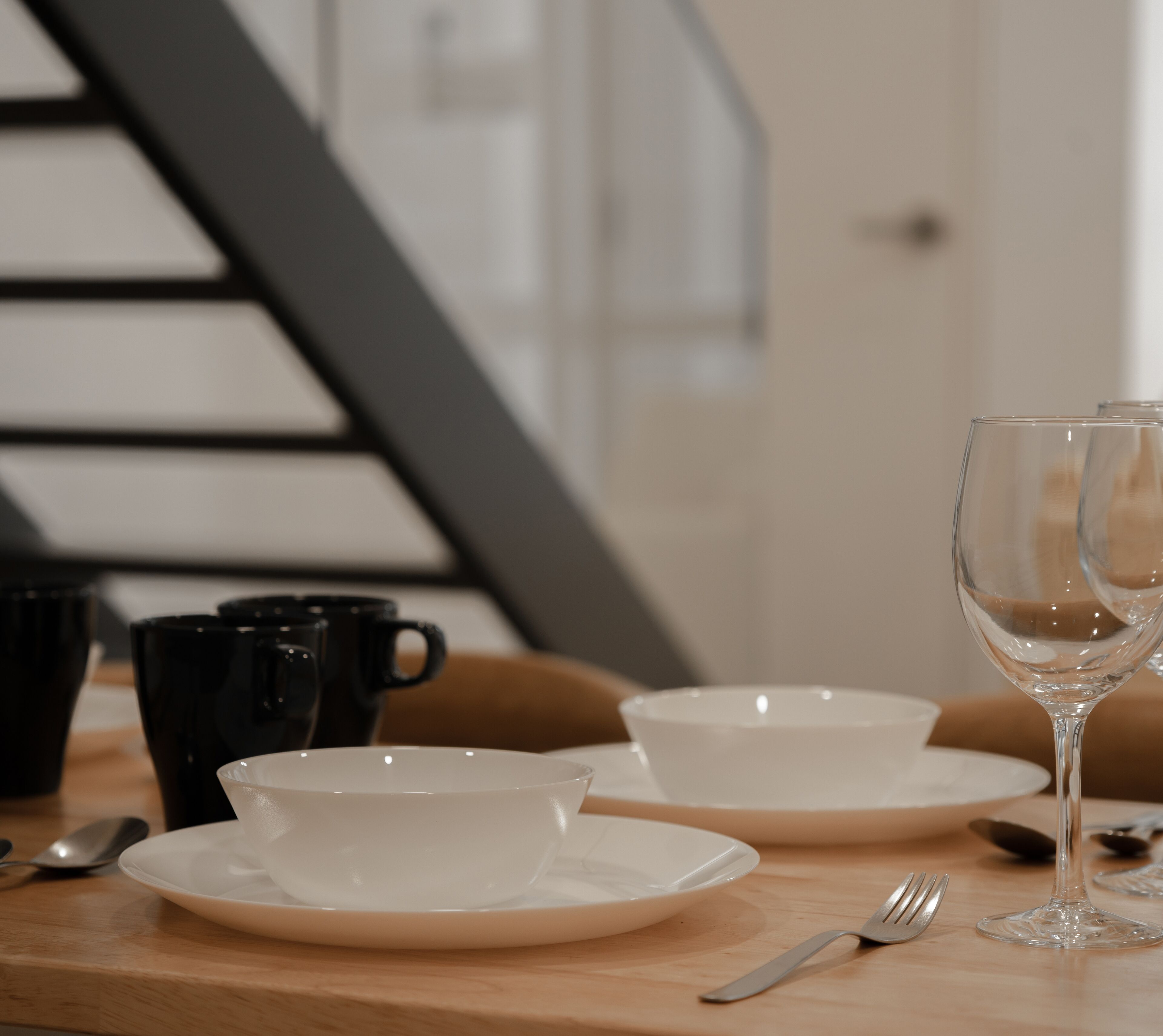 A dining table with white plates, black cups, and a wine glass.