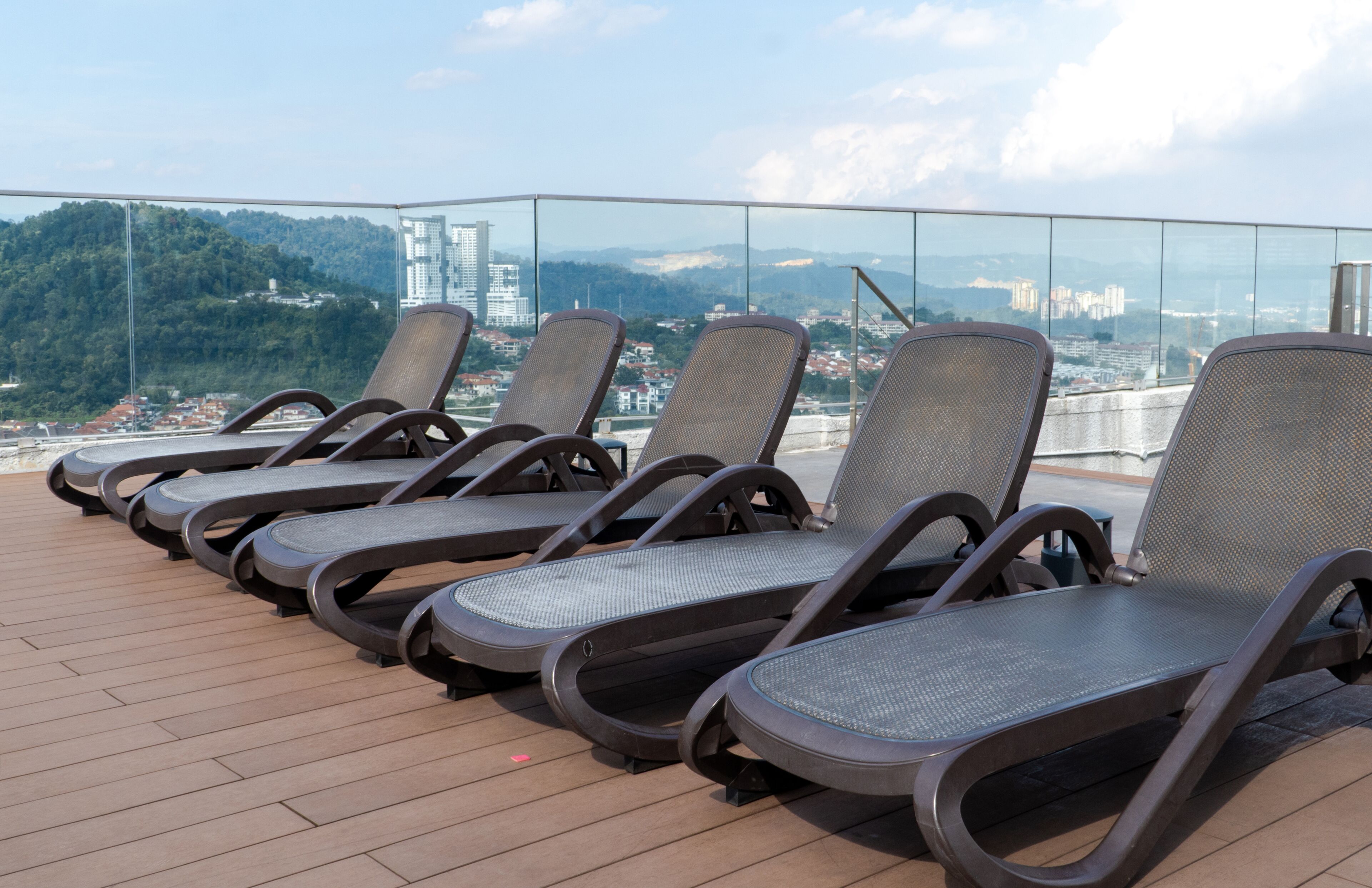A row of sun loungers on a wooden deck with a cityscape view in the background.