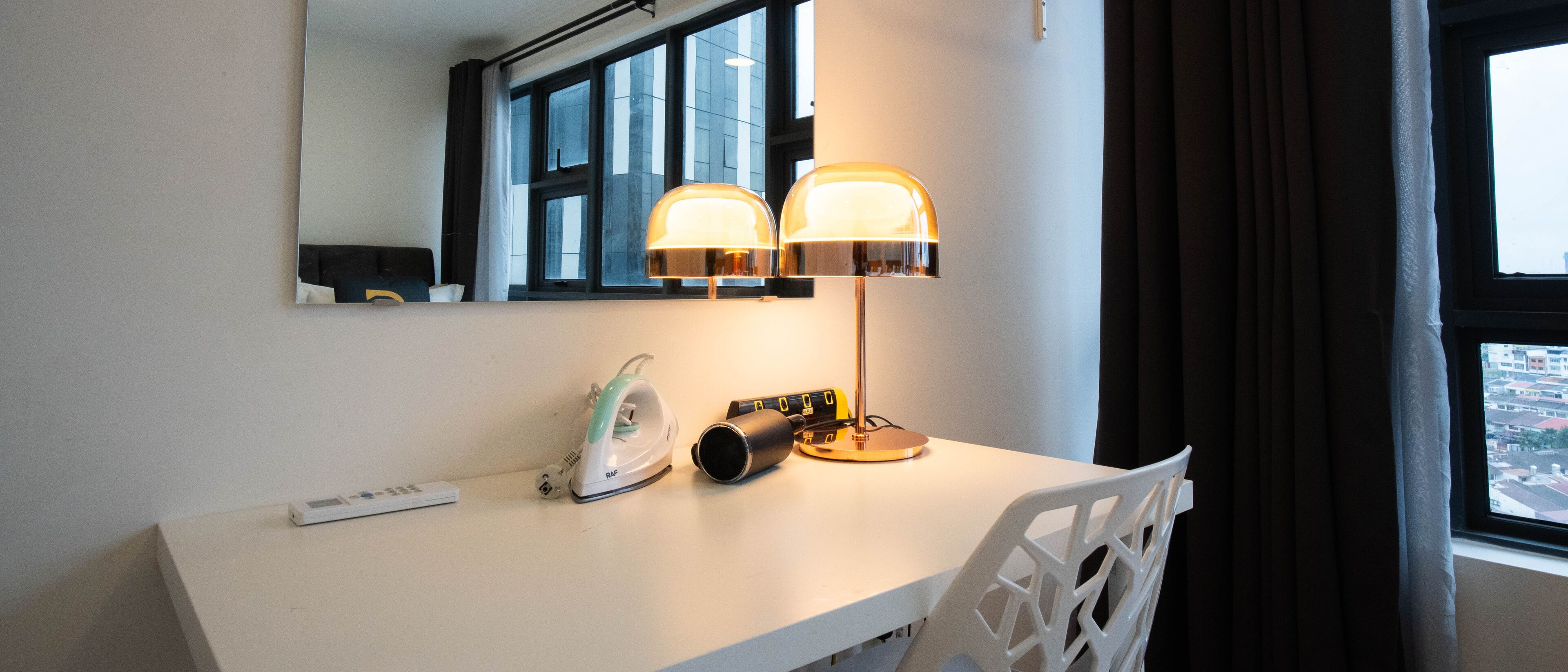 Una camera d'albergo con una scrivania bianca, una lampada, un ferro da stiro e un telecomando.