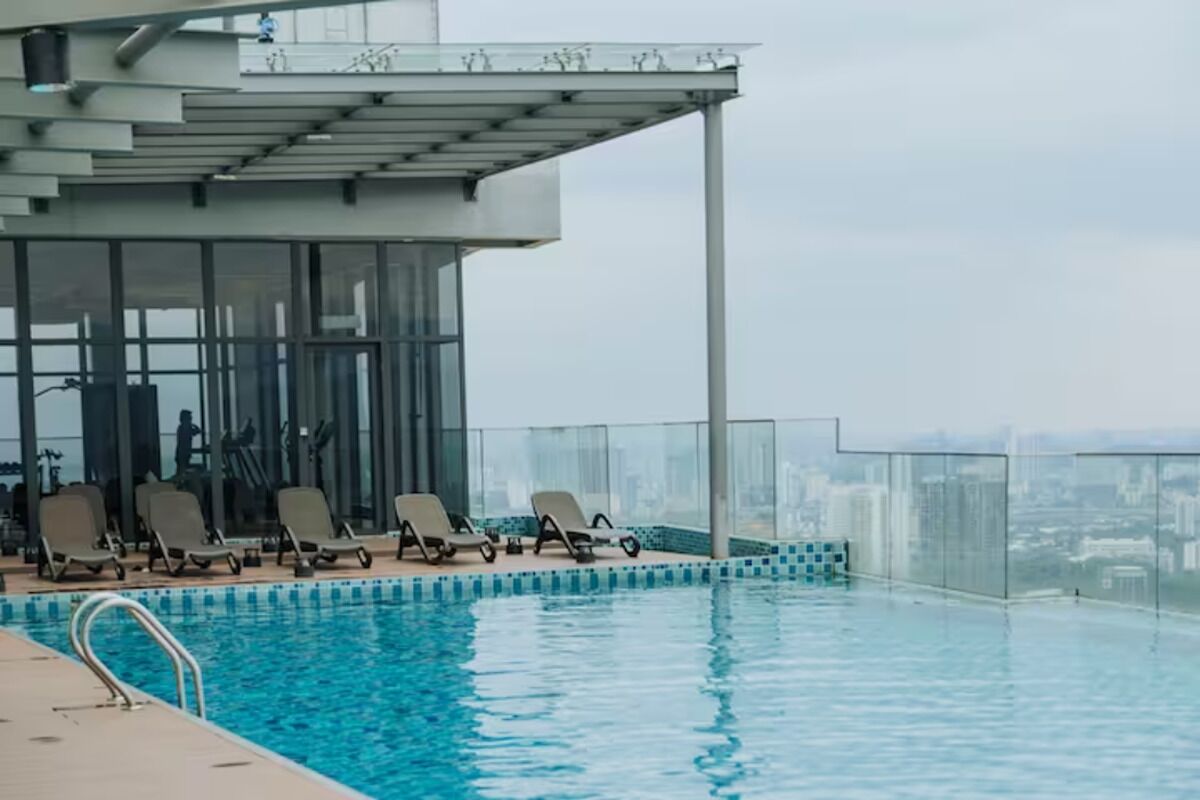 Een overloopzwembad binnen met ligbedden en fitnessapparatuur, omgeven door een glazen balustrade en uitzicht op de stad.