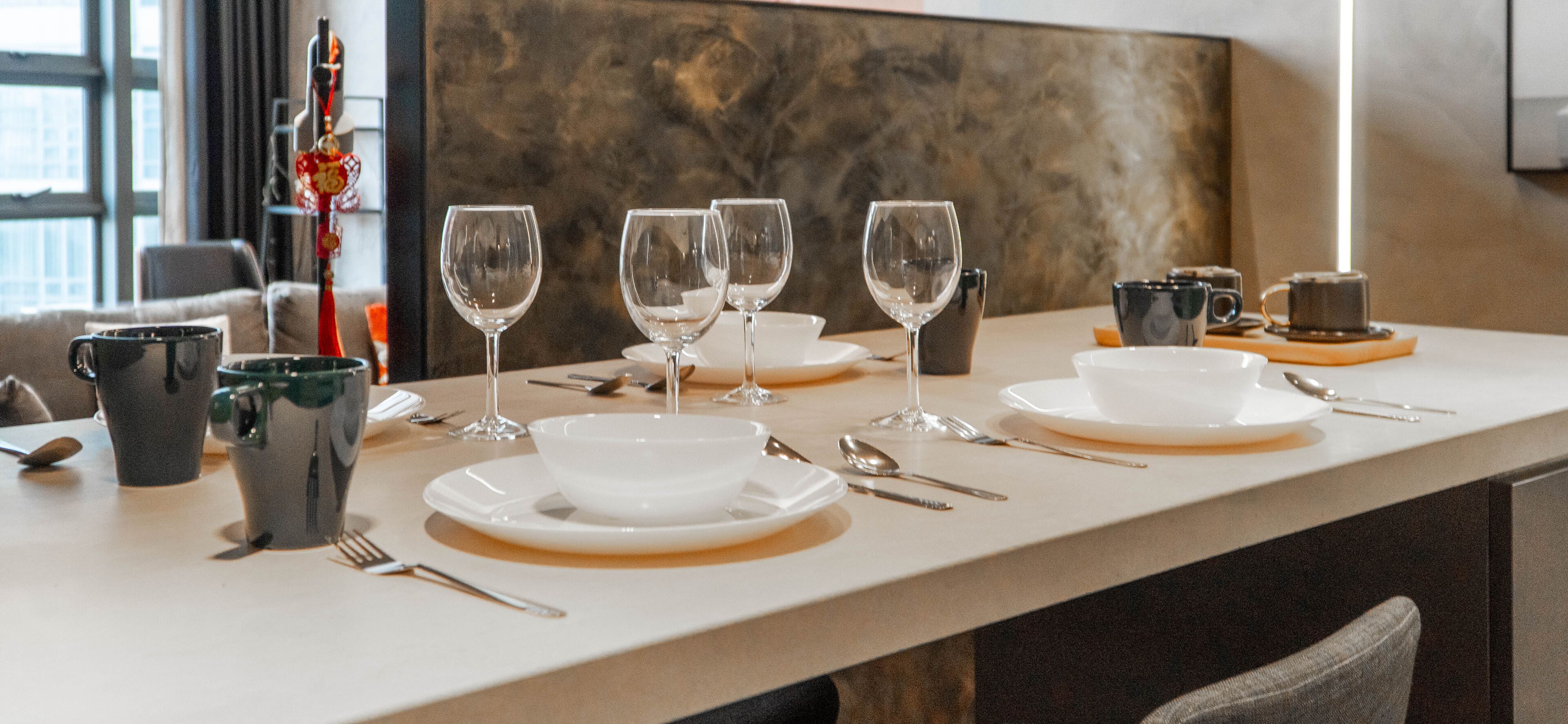 Una mesa de comedor dispuesta con platos, tazones y cubiertos blancos, y algunas copas de vino.
