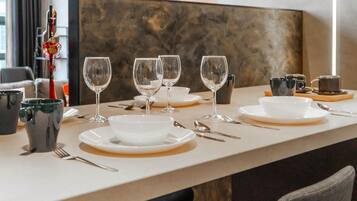 Una mesa de comedor dispuesta con platos, tazones y cubiertos blancos, y algunas copas de vino.