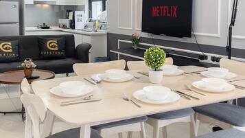 A modern hotel room with a dining area, a sofa with 'Guestonic' branding, a TV displaying 'NETFLIX', and a small potted plant.