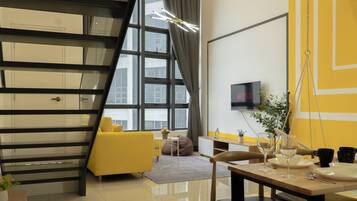 A modern living room with a yellow sofa, a dining table set with wine glasses, and a TV mounted on the wall.