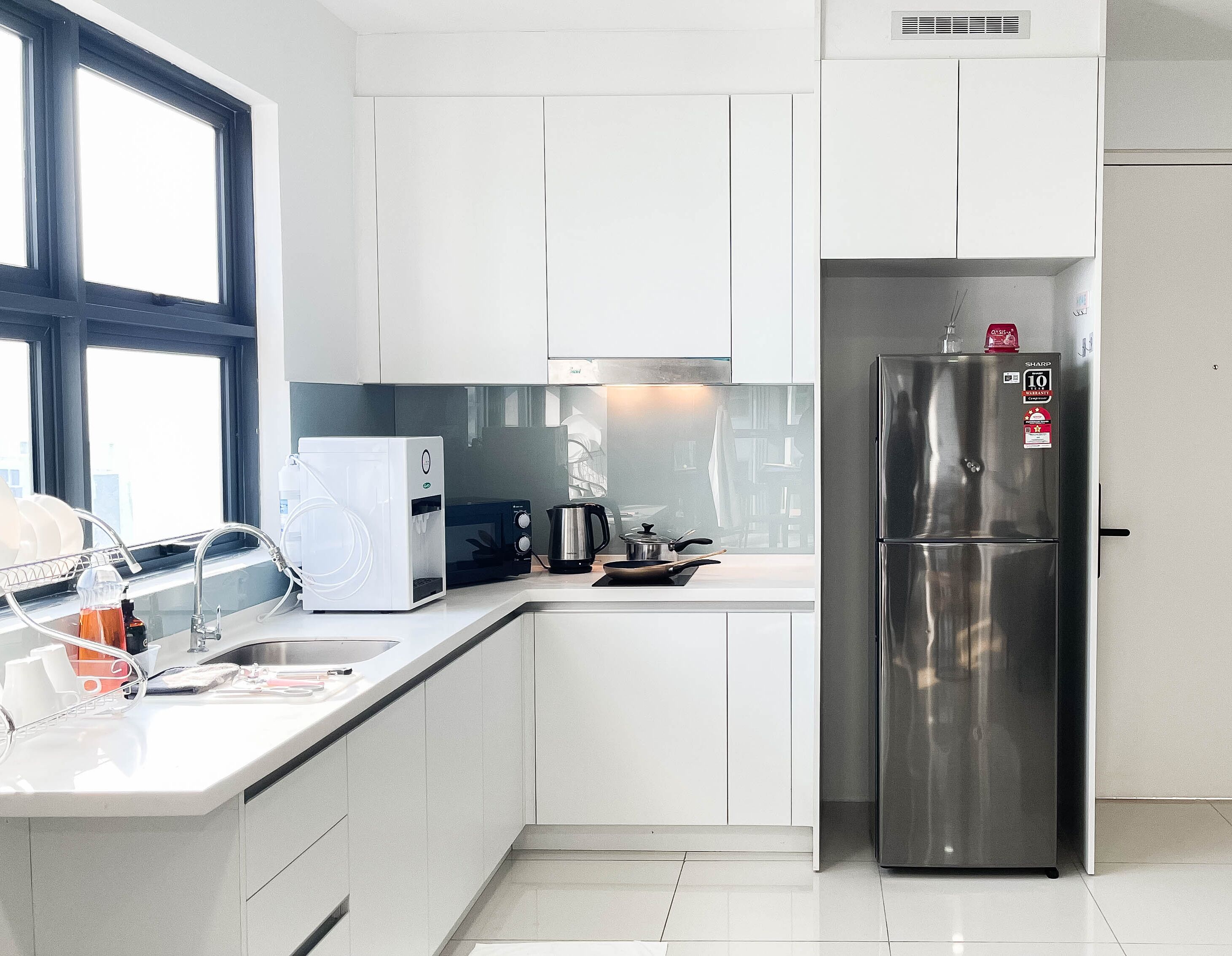 Una cocina moderna con armarios blancos, un refrigerador de acero inoxidable, una cafetera y un hervidor.
