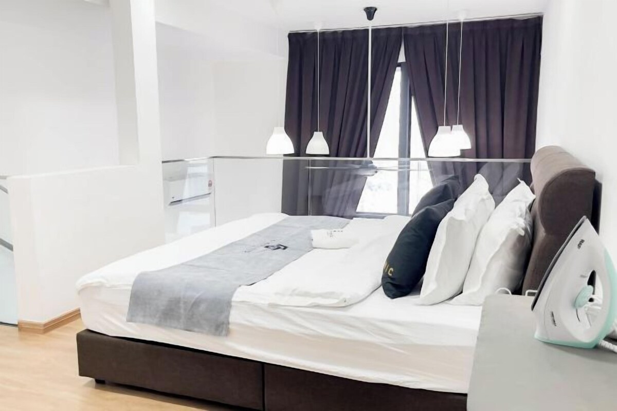 Une chambre d’hôtel moderne, équipée d’un lit, d’une table de chevet avec un fer à repasser, et offrant une vue sur l’extérieur grâce à une fenêtre avec des rideaux.