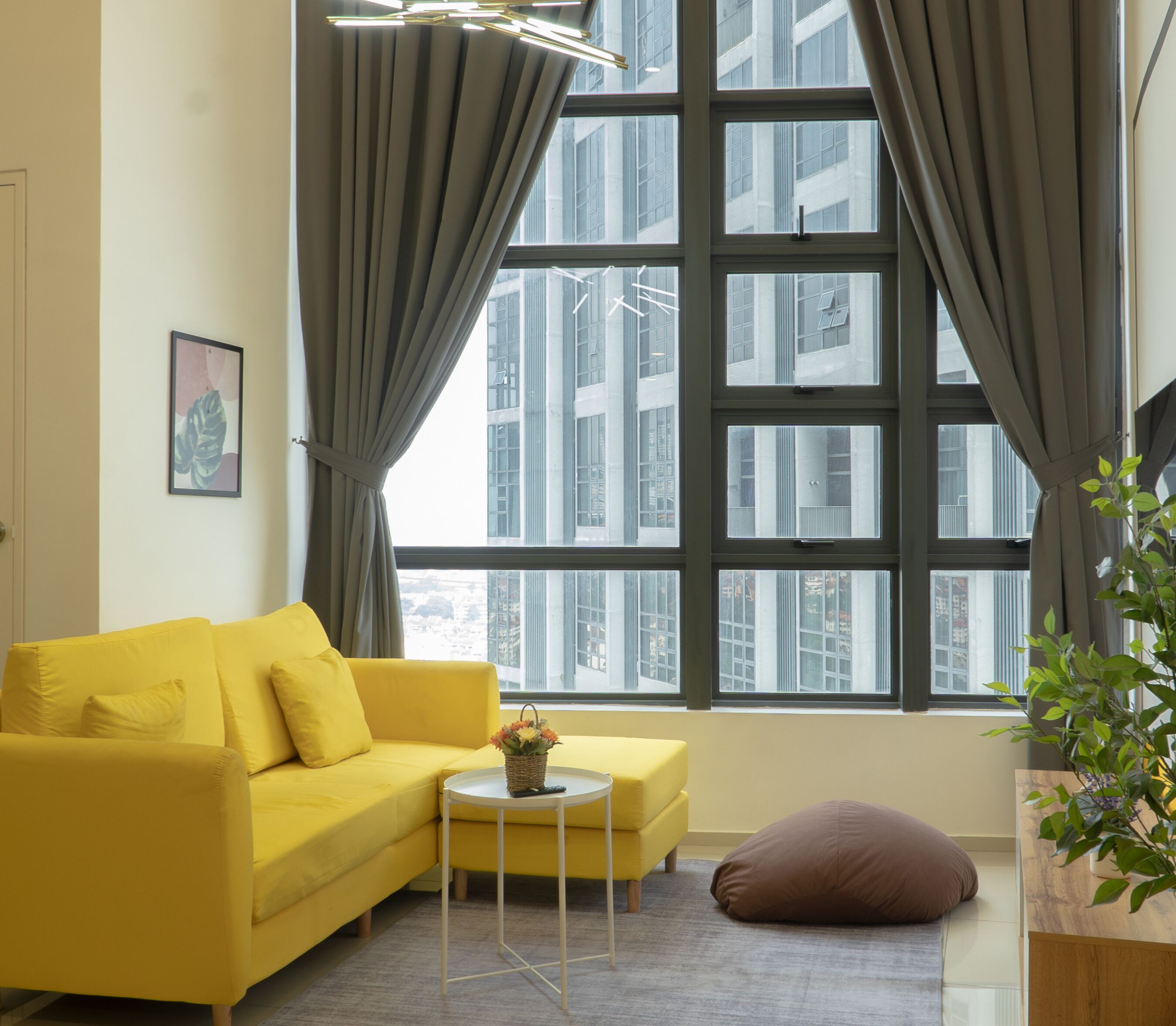 A modern living room with a yellow sofa, a small round table, and a large window with curtains.