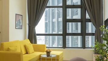 A modern living room with a yellow sofa, a small round table, and a large window with curtains.