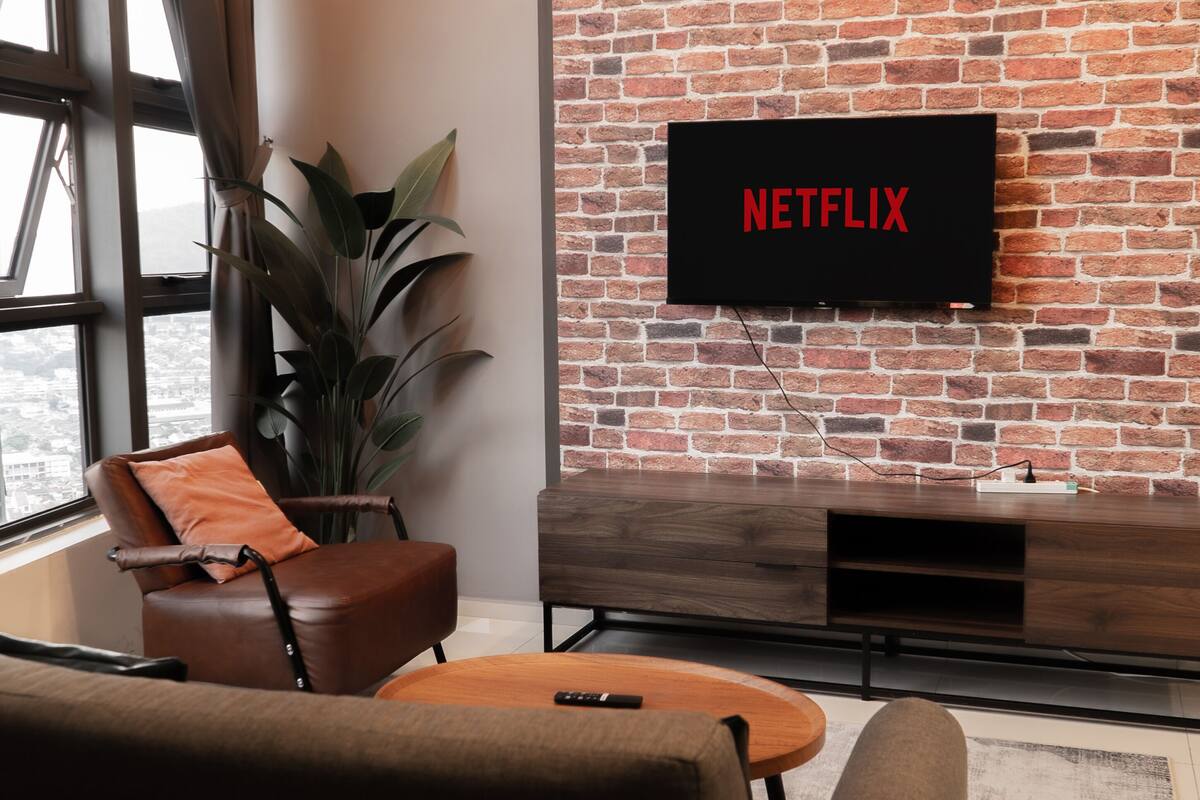 Un salon avec un mur en briques, un téléviseur fixé au-dessus d’un meuble en bois et une grande fenêtre.