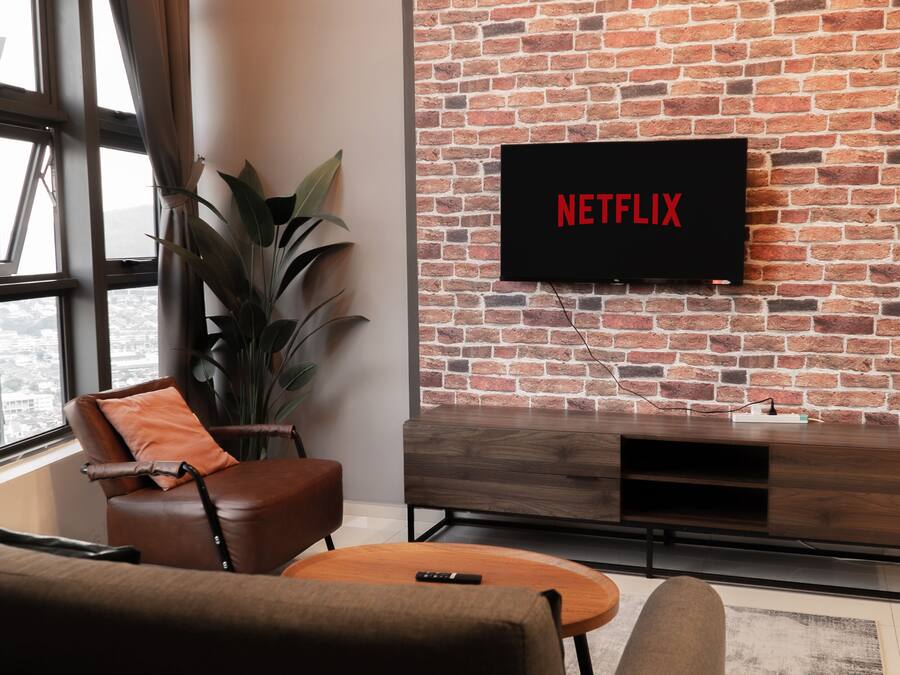 A living room with a brick wall, a TV mounted above a wooden cabinet, and a large window.