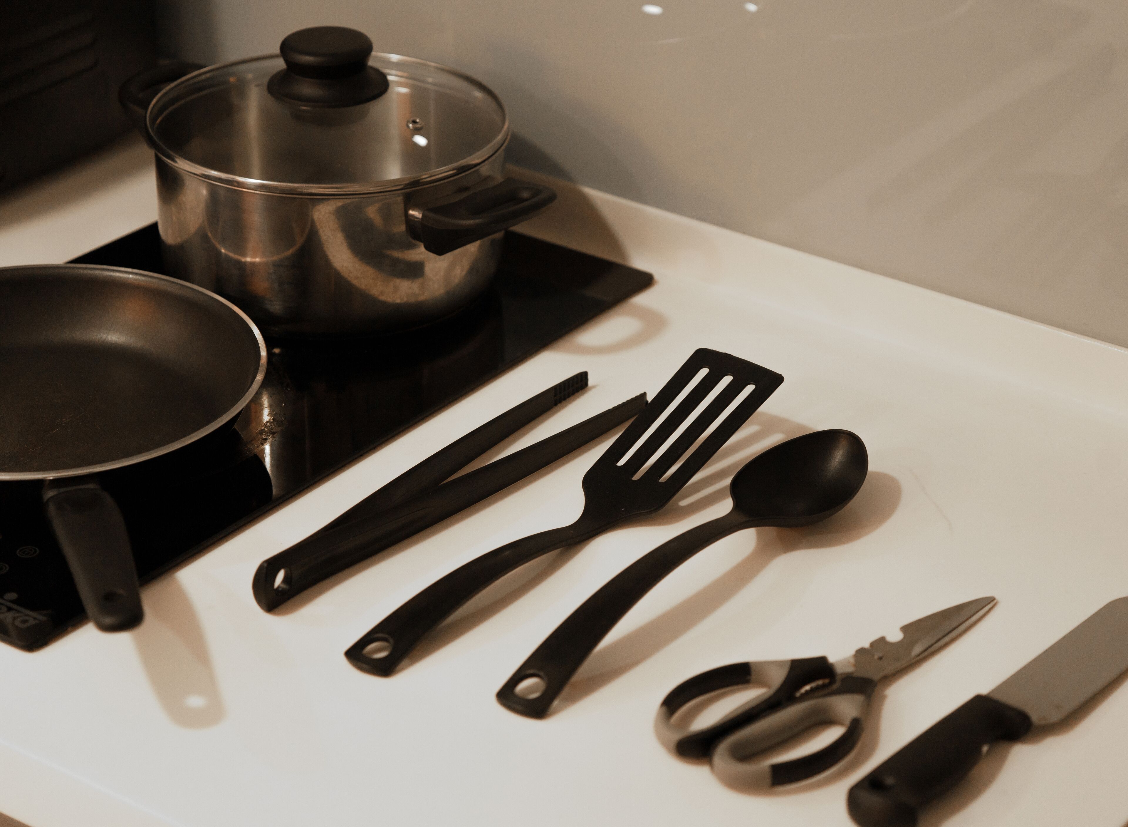 A kitchen counter with a frying pan, spatula, spoon, scissors, and a knife.