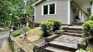 A two-story house with a front porch, a wooden staircase, and a small deck.