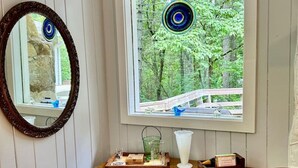 A room with a wooden dresser, a mirror, and a window with a view of a forest.