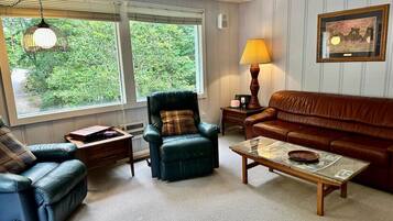 A living room with a leather sofa, a green armchair, a blue armchair, a wooden coffee table, and a lamp.