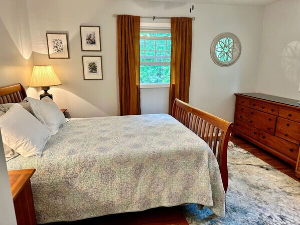 Un dormitorio con cama, cómoda, lámpara y ventana con cortinas.