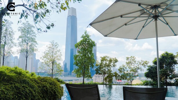A view of a city skyline with modern skyscrapers, a body of water, and a deck with two chairs and an umbrella. - Guestonic Continew Comfy Home (Kuala Lumpur)