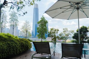 Vista de un horizonte urbano con rascacielos modernos, una masa de agua y una terraza con dos sillas y un paraguas.
