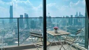 A balcony with a table and chairs, overlooking a cityscape with various buildings. - Guestonic Continew Comfy Home (Kuala Lumpur)