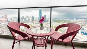 A round glass table with two wicker chairs, a vase with a pink flower, and a cityscape view through large windows. - Guestonic Continew Comfy Home (Kuala Lumpur)
