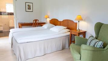 Habitación de hotel con cama doble, dos mesitas de noche con lámparas, un sillón verde y un escritorio pequeño con una silla.