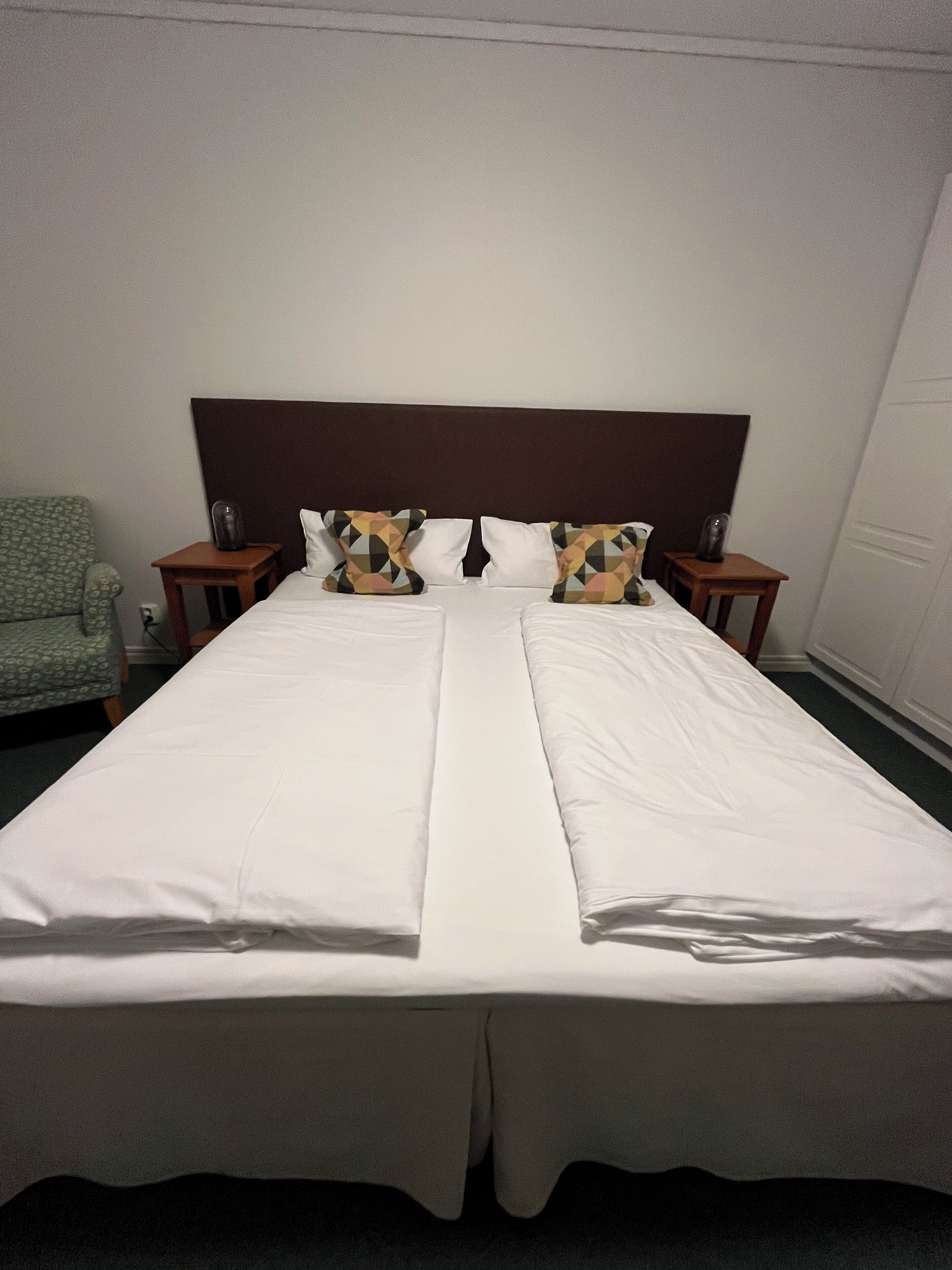 A double bed with white linens, a dark headboard, and two nightstands with lamps.