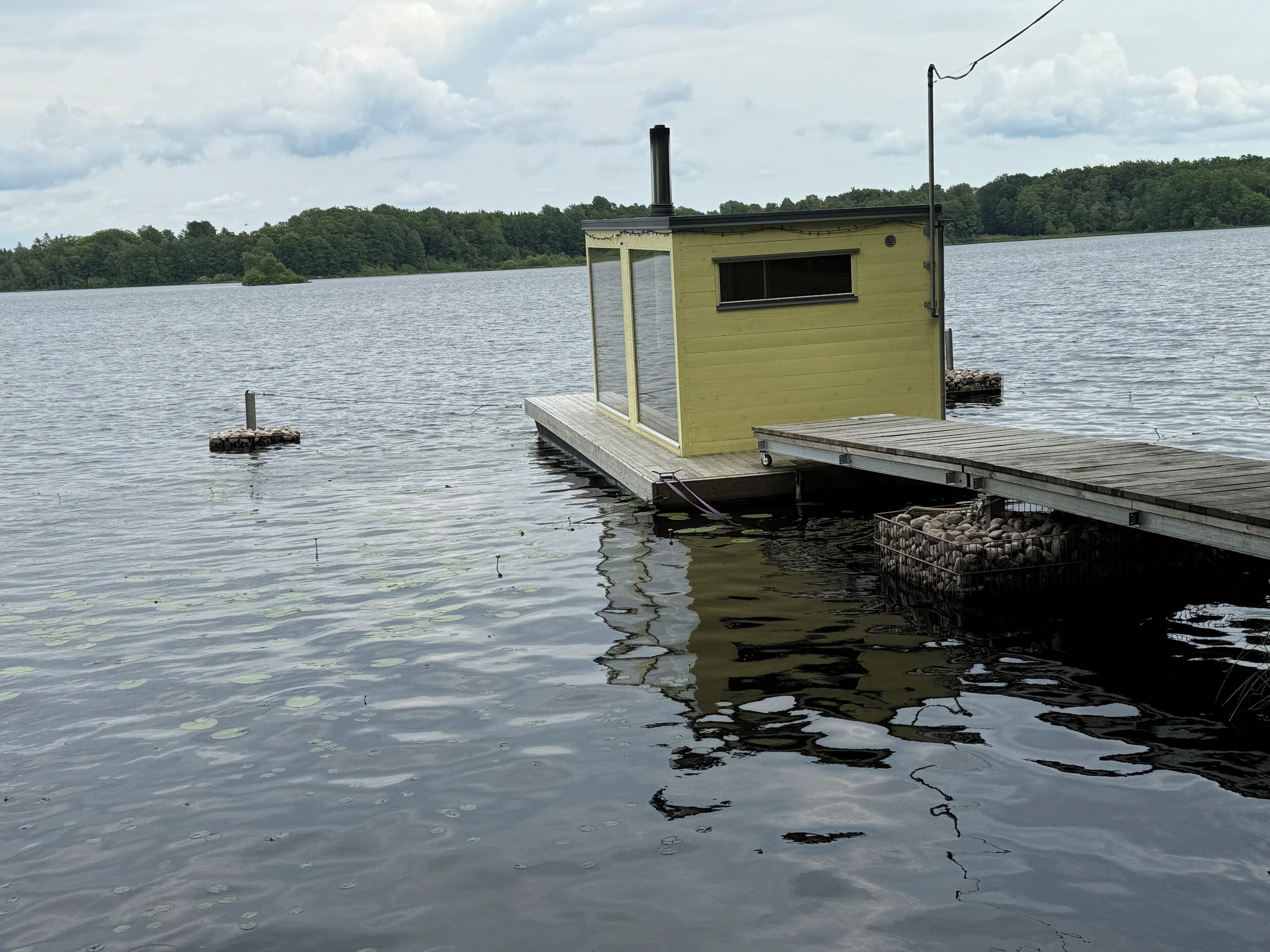 Un pequeño muelle amarillo con una cabaña sobre un lago tranquilo, rodeado de árboles.