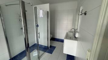 Ett badrum med en dusch som är avskärmad med glasväggar, ett vitt handfat och en toalett.
