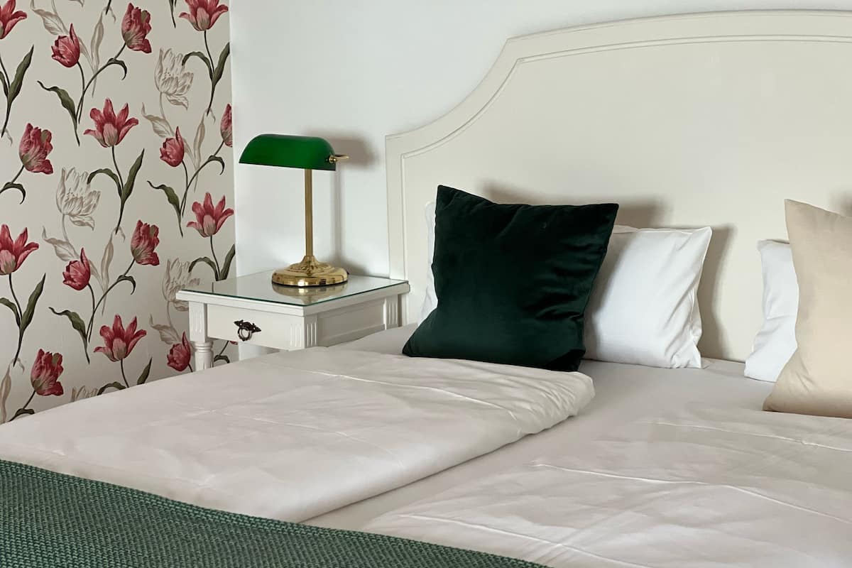 Uma cama bem arrumada com lençóis brancos, um cobertor verde e uma luminária verde em uma mesa de cabeceira.