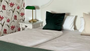 Una cama bien hecha con ropa blanca, un plaid verde y una lámpara verde sobre una mesita de noche.