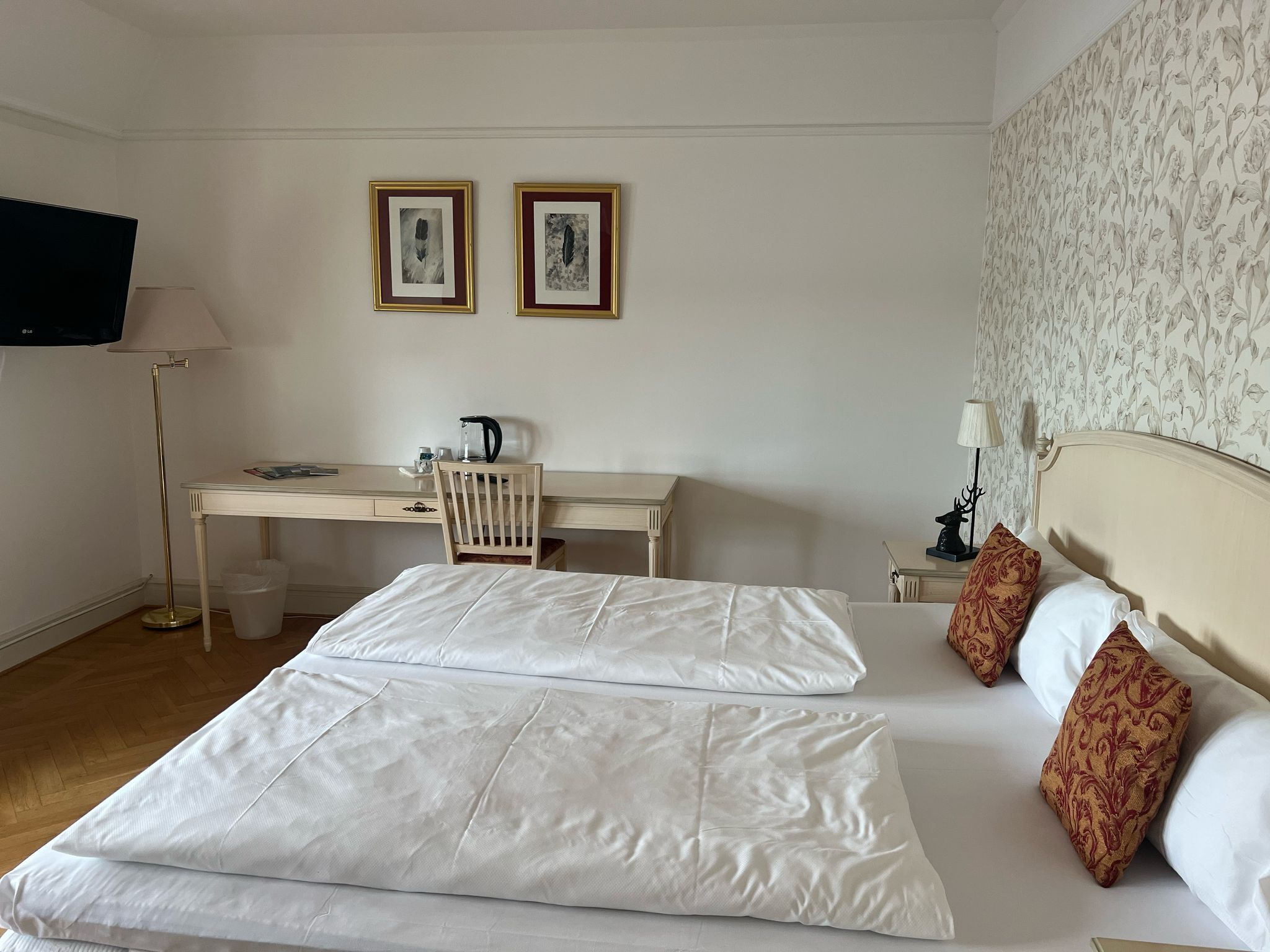 Ein Hotelzimmer mit einem Bett, einem Schreibtisch und zwei gerahmten Bildern an der Wand.