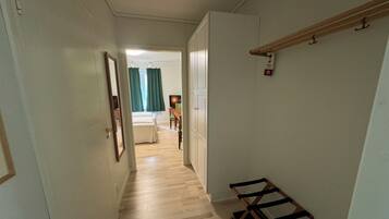 A narrow hallway with a wooden floor, a coat rack, and a bed in the background.