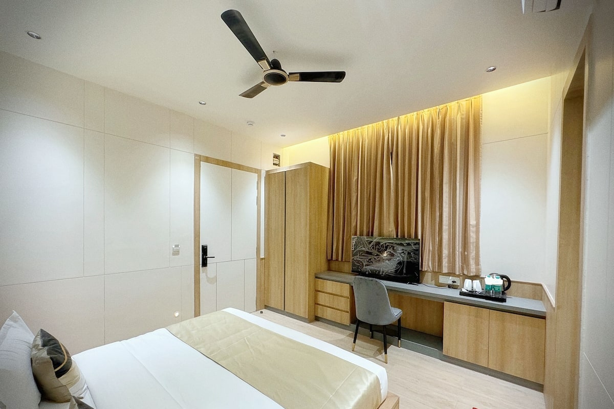 A modern hotel room with a bed, a desk, a chair, a ceiling fan, and a window with curtains.