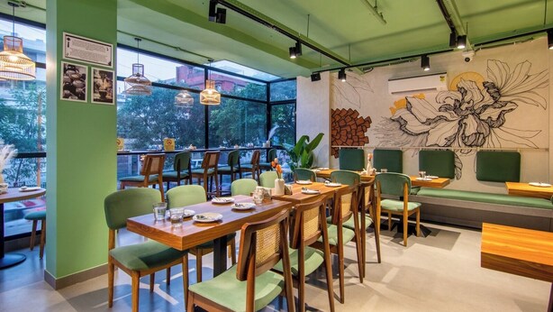 A restaurant with wooden tables and chairs, large windows, and a mural on the wall. - ASAR by Orion Hotels (New Delhi)