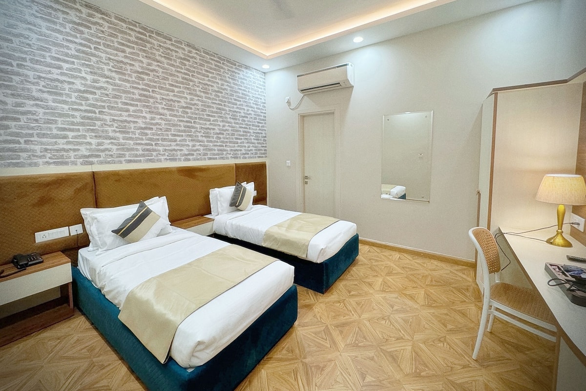 A hotel room with two beds, a desk, a chair, a ceiling fan, and a brick-patterned wall.