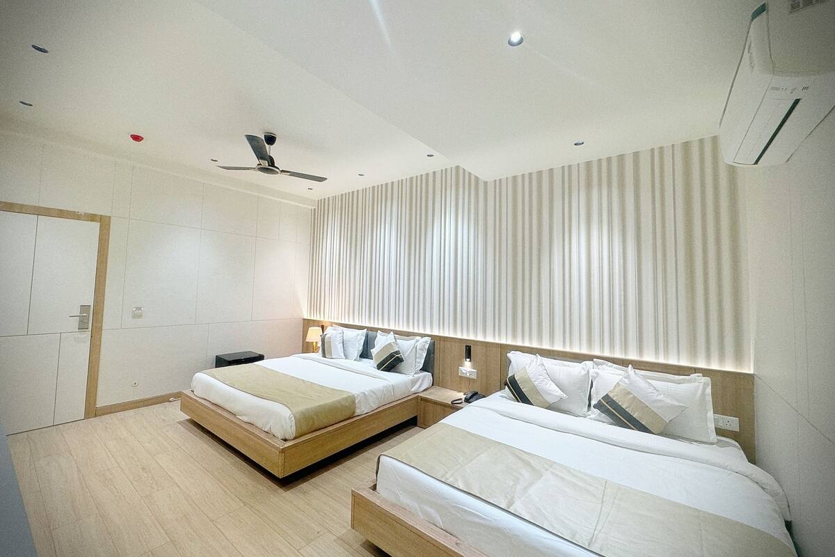 A modern hotel room with two single beds, a ceiling fan, and a large window with curtains.