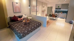 A modern bedroom with a large bed, a small table, and a dining area with chairs. - Guestonic Netizen Cozy Studio (Cheras)