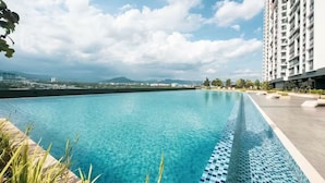 A swimming pool with clear blue water, surrounded by a modern building and a view of distant mountains. - Guestonic Netizen Cozy Studio (Cheras)