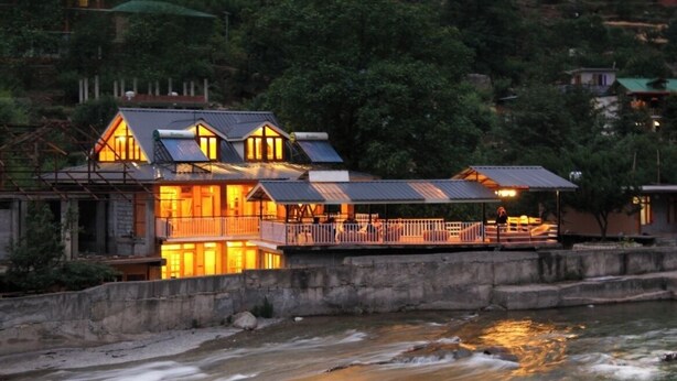 A riverside property with a prominent building featuring a balcony and a covered area. - Virman Riverside Resort (Banjar)