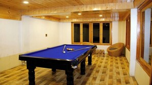 A pool table in a room with wooden ceiling and walls, a checkered floor, and a window with a wicker chair outside. - Virman Riverside Resort (Banjar)