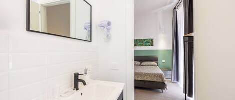 A modern bathroom with a white sink, mirror, and two wall-mounted hair dryers.